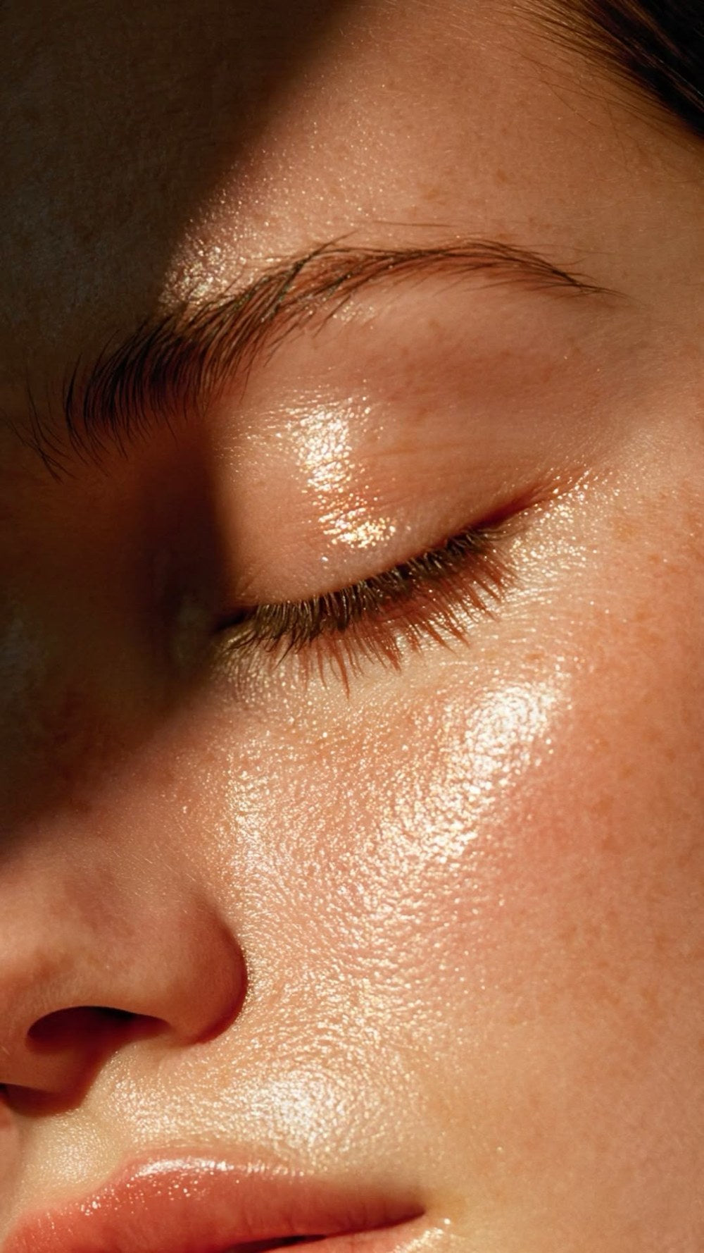 Close-up of a woman's closed eye and cheek, her skin glowing in warm light