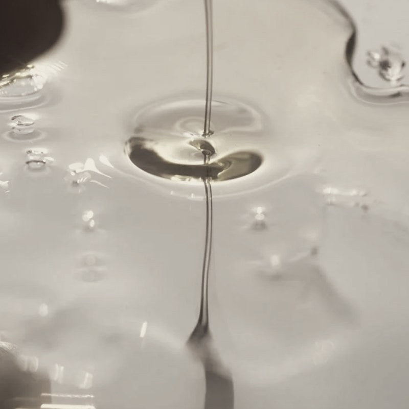 Golden oil pouring into a pool of clear liquid