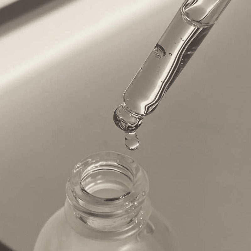 A dropper releasing a drop of clear liquid above a frosted glass bottle
