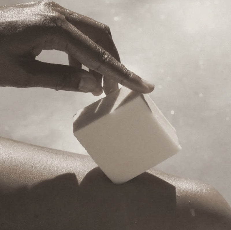 A hand holding a cream-colored block of soap against bare skin